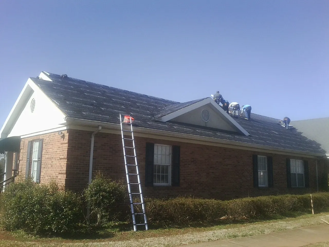 Crew tearing shingles off a brick ranch roof with a ladder set — Metal Roof Repair work by our crew in Vermont