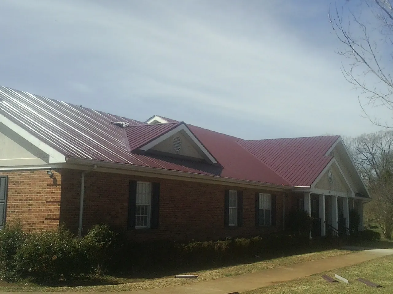 Red metal roof with gabled entries on a long brick building, from a Hail Damage Roof Repair job in Vermont