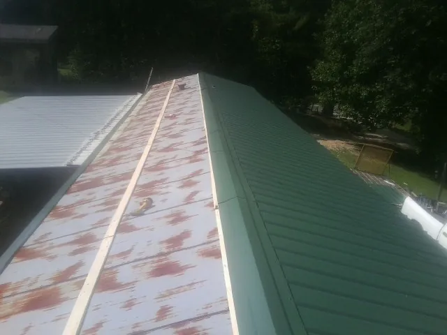 Old rusted panels beside newly installed green metal roofing — Wind Damage Roof Repair by Roofing Brothers in Vermont