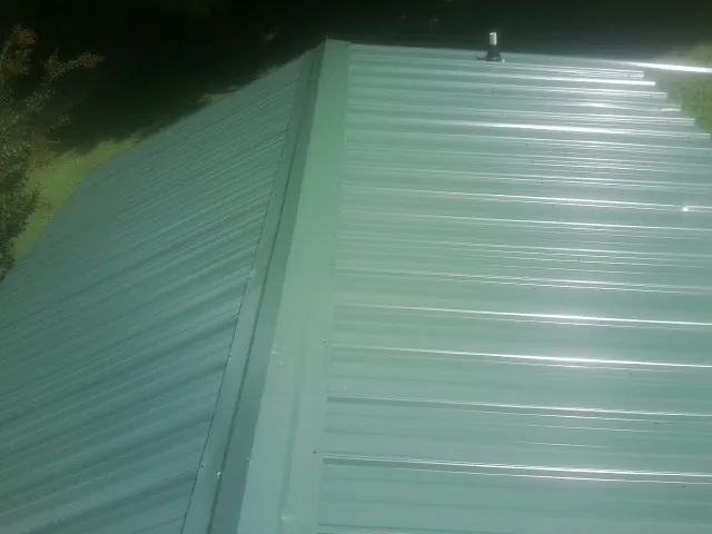 New green metal panels meeting at the ridge of a roof — Flat Roof Repair work by our crew in Vermont