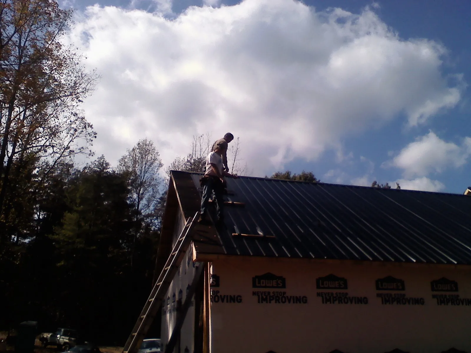 Roofer fastening dark metal panels high against a cloudy sky, from a Roof Inspection job in Vermont