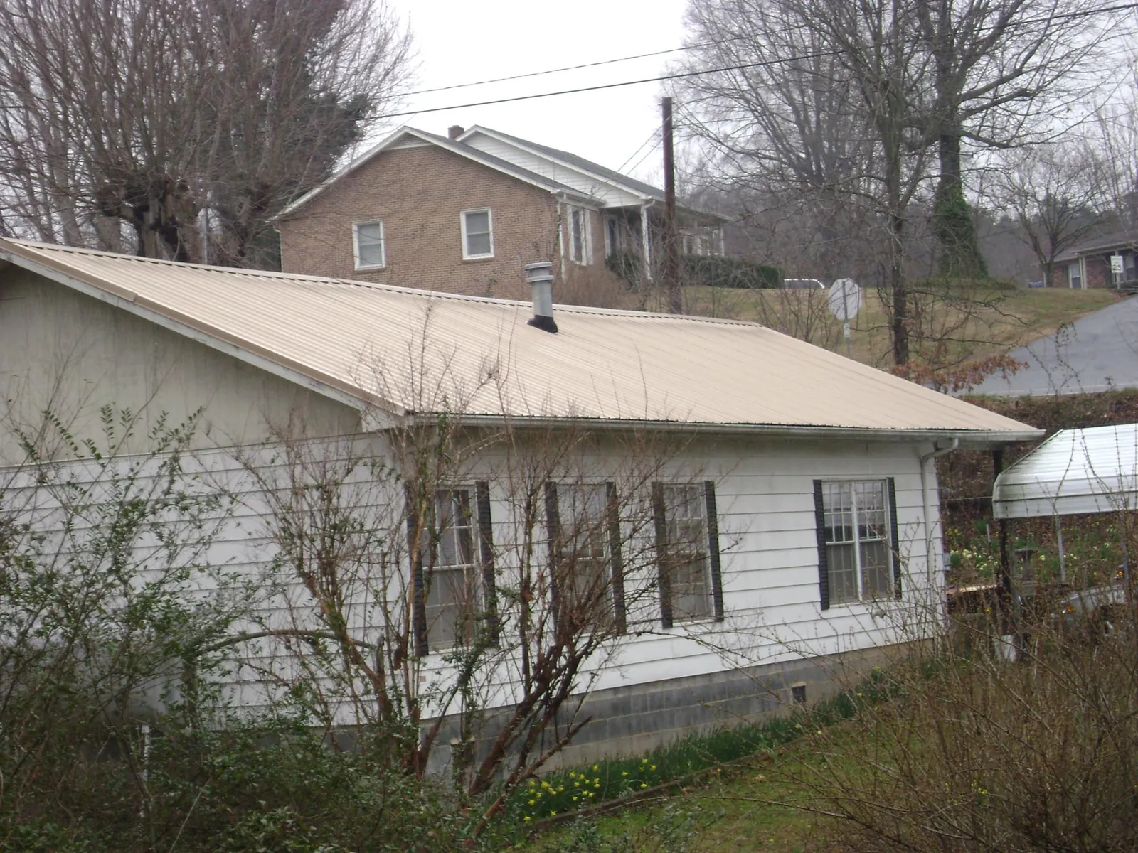 Tan metal roof on a white sided house set into a hillside — Commercial Roofing by Roofing Brothers in Vermont