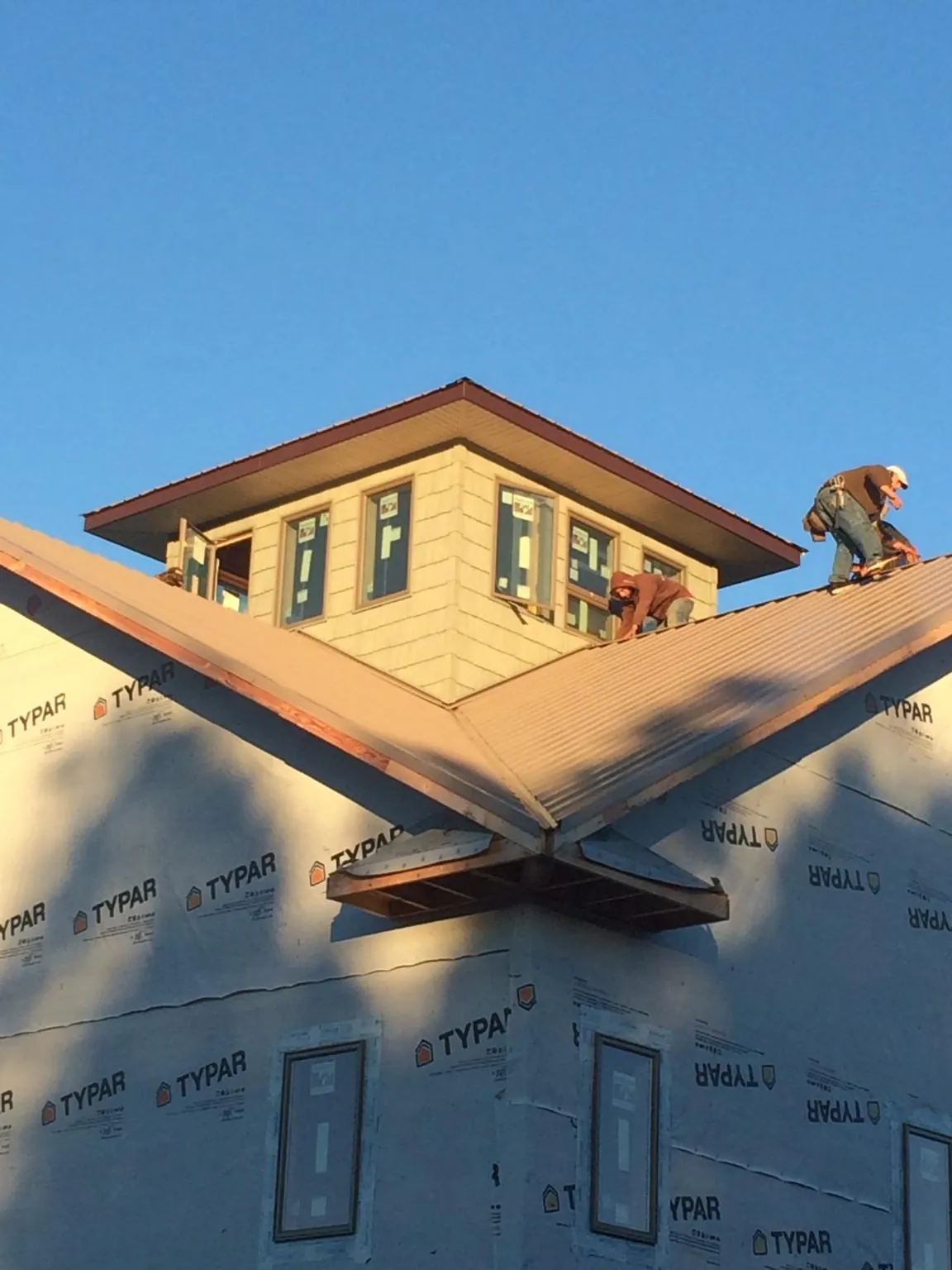 Roofers working around a rooftop cupola on a new metal roof at sunset — Roof Waterproofing in Vermont by Roofing Brothers